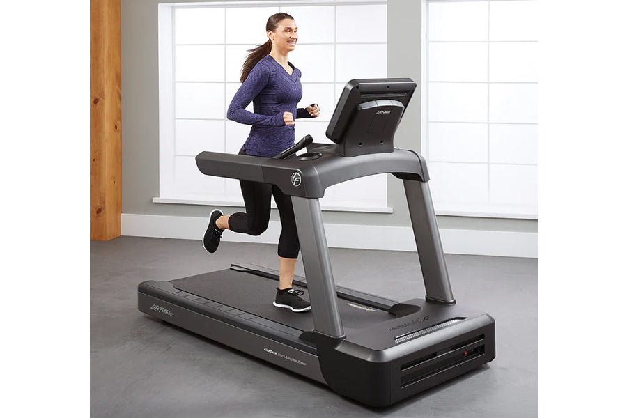 Woman running on Life Fitness Club Series Plus treadmill with digital display, wearing purple long-sleeve top and black capri