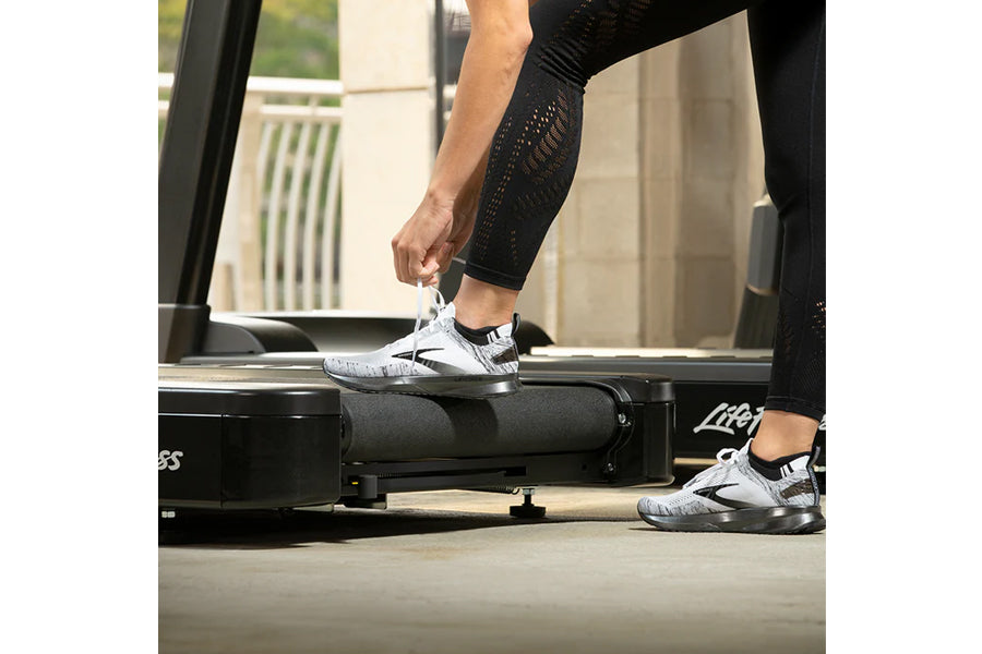 Person wearing black textured leggings and white sneakers using Life Fitness treadmill in gym studio setting