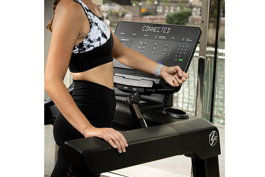 Black and white tie-dye racerback sports bra with black high-waist leggings worn by model on Life Fitness treadmill with digi