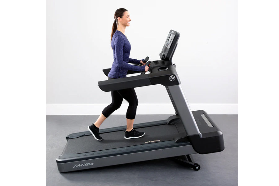 Woman running on black and gray Life Fitness treadmill with digital display, wearing navy long-sleeve shirt and black capri l