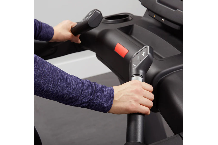 Person wearing navy sleeve holding black treadmill handlebar with digital display and red emergency stop button