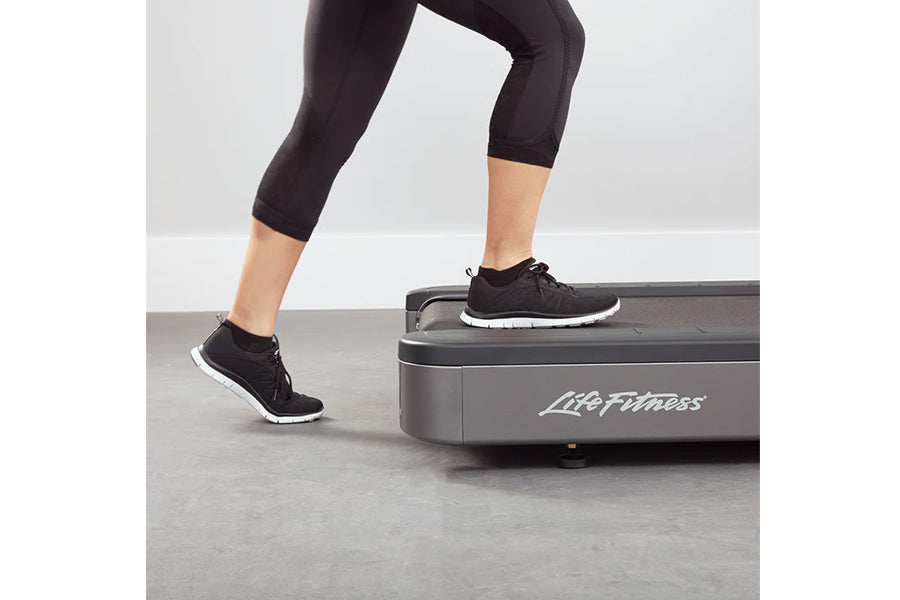 Woman wearing black capri leggings and black sneakers with white sole, exercising on Life Fitness treadmill