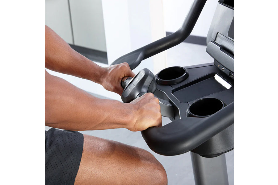 Hands gripping handlebar of stationary exercise bike with black frame and curved display console