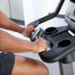 Person's hands gripping black handlebar on upright stationary exercise bike with dual cup holders and digital console
