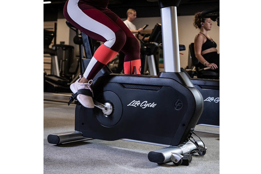 Person wearing burgundy and white colorblock leggings using black Life Cycle upright stationary bike in gym setting