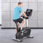 Man wearing turquoise t-shirt and black shorts exercising on black and silver upright stationary bike with digital display co