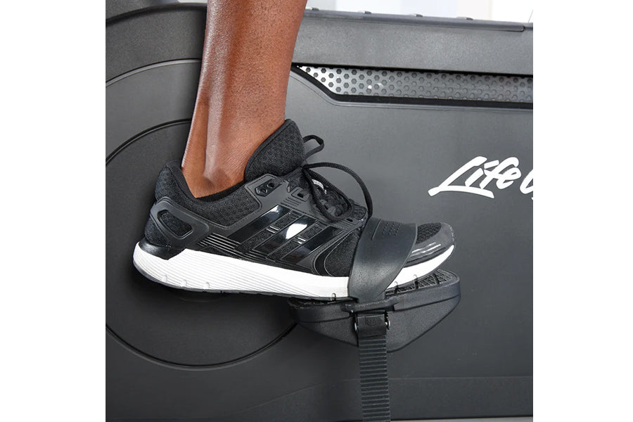 Black and white running shoe with lace-up design worn on exercise bike pedal, lifestyle shot