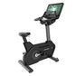 Black upright stationary exercise bike with digital display console showing fitness content, adjustable seat, and gray pedal 