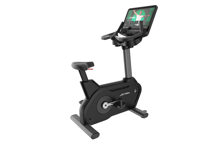 Black upright stationary exercise bike with digital display console showing fitness content, adjustable seat, and gray pedal 