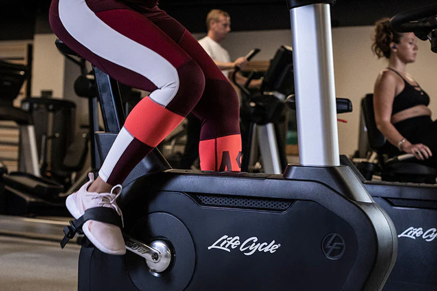 Burgundy, white and coral colorblock leggings worn by model on stationary bike in gym setting