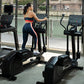 Woman wearing coral sports bra and navy leggings with stripe detail using black Life Fitness elliptical in modern gym with la