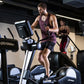 Man wearing burgundy tank top and black shorts exercising on Life Fitness elliptical machine in gym setting with other equipm