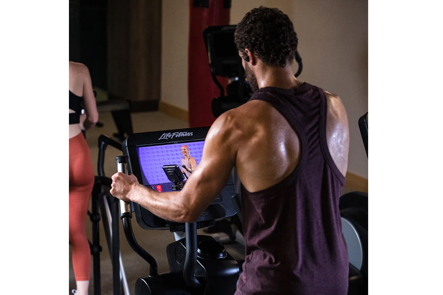 Man using Life Fitness Club Series elliptical machine with digital display during workout, wearing burgundy sleeveless tank t