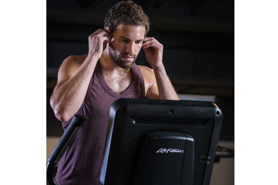 Man wearing burgundy sleeveless tank top using black Life Fitness elliptical machine, indoors