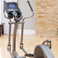 Life Fitness E1 elliptical cross-trainer with black console, gray frame and handlebars, displayed in home gym setting with br