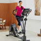 Woman in magenta t-shirt using black and gray Life Fitness elliptical machine with digital display in home gym setting