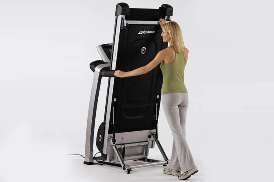 Woman in olive tank top using black and silver Life Fitness folding treadmill on white background