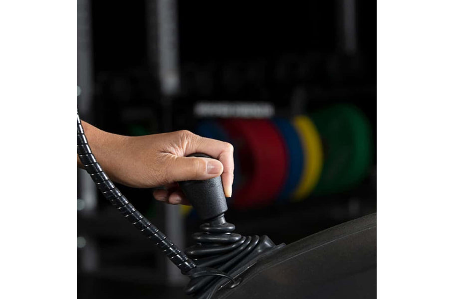 Hand gripping black rubber handle of Life Fitness elliptical machine in gym setting with weight plates blurred in background
