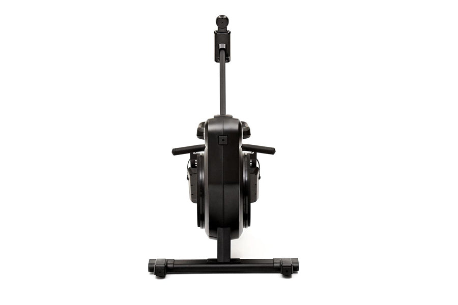 Black stationary rowing machine with vertical monitor arm, dual foot pedals, and horizontal footrest on white background
