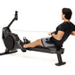 Black magnetic rowing machine with digital monitor, shown with male model in black shirt and gray shorts demonstrating rowing