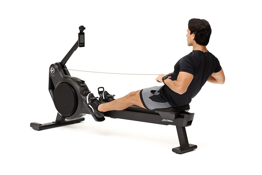 Black magnetic rowing machine with digital monitor, shown with male model in black shirt and gray shorts demonstrating rowing