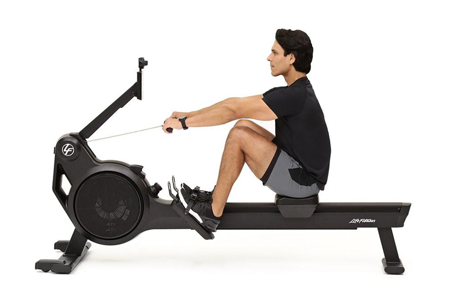 Man seated on black rowing machine with extended arms pulling handle, demonstrating proper form on white background