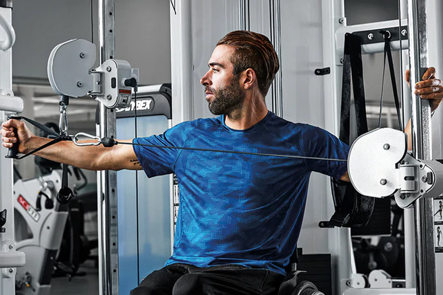 Man wearing blue patterned athletic shirt using dual adjustable pulley machine in gym setting