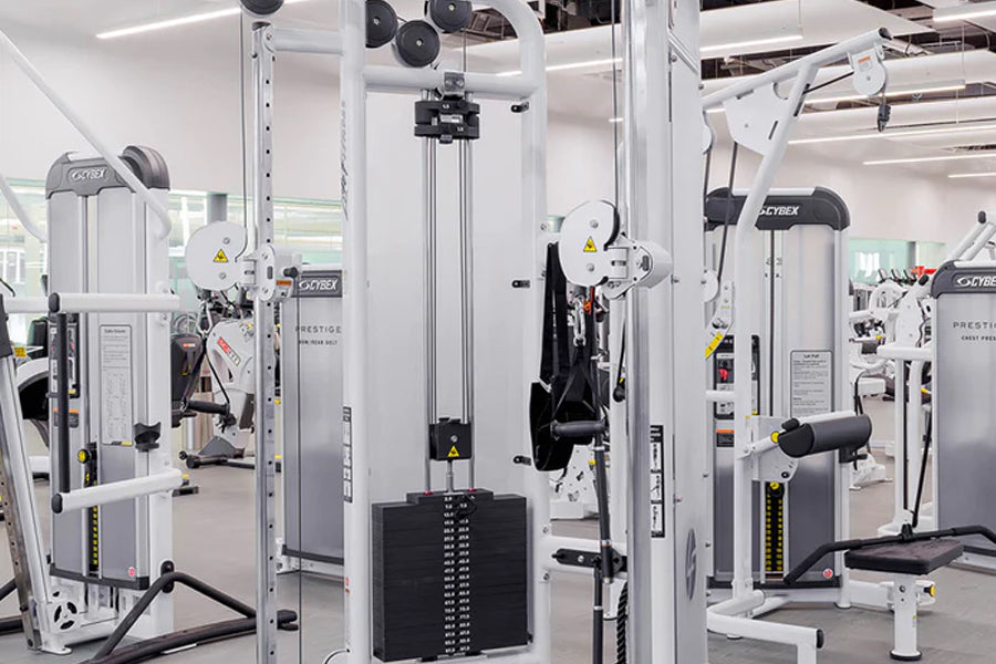 White and black Cybex strength training machines with adjustable pulleys in a modern gym setting