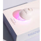 White and pink LED light therapy device with silicone contact head, displayed in product packaging on white background