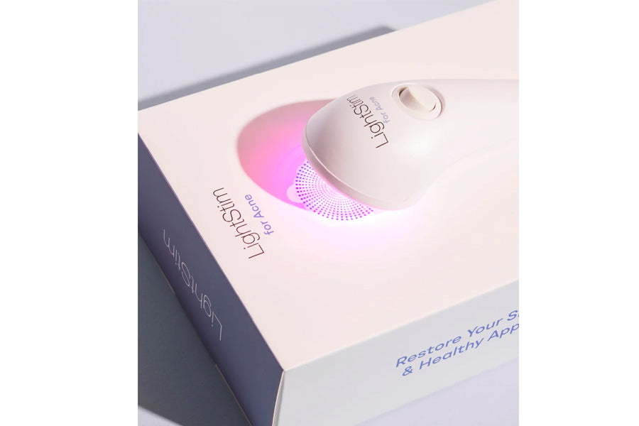 White and pink LED light therapy device with silicone contact head, displayed in product packaging on white background