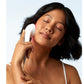 White handheld LED light therapy device used on cheek, worn by model with dark hair against light blue background