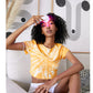 Model wearing yellow and white tie-dye crop t-shirt, holding pink LED light therapy device near face