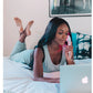 Woman lying on bed in gray sleeveless tank top using LightStim LED light therapy device while working on laptop