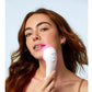 Woman with reddish-brown hair holding white LightStim LED light therapy device with pink light against chin, on light blue ba