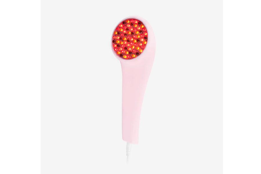 Pink handheld LED light therapy device with red and amber illuminated bulbs on circular head, white cord, on white background