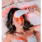 Woman using white LED light therapy device on forehead, emitting red and orange light, worn on bed with pink pillows