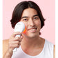 Man holding white LED light therapy device with red light glow near his face against pink background