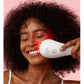LightStim LED light therapy device with red light emitting from white handheld applicator, held against model's cheek on pink