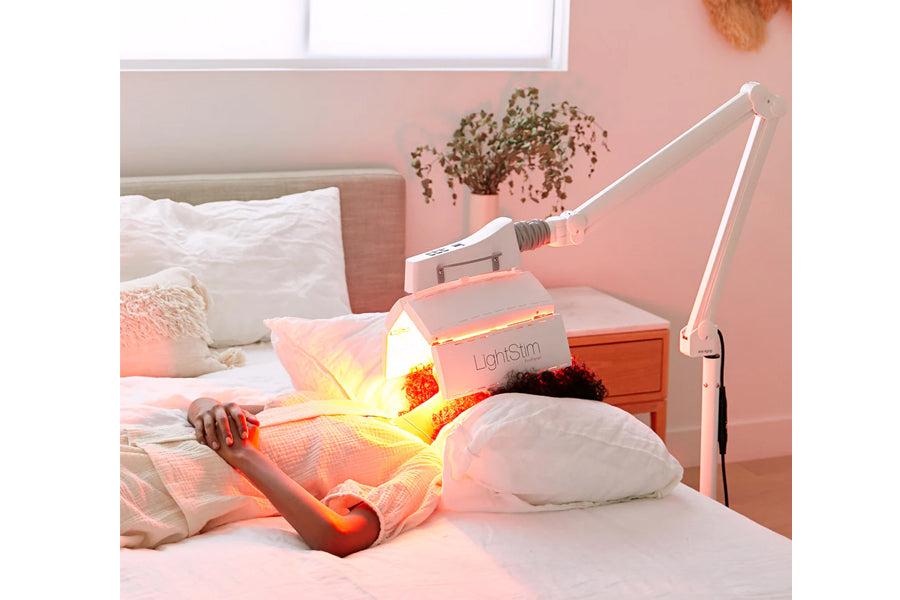 LightStim ProPanel LED light therapy lamp with red and yellow illuminated panel on bedroom nightstand, adjustable white arm a