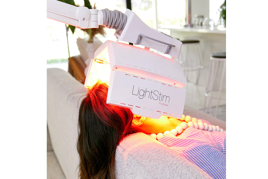 LightStim ProPanel LED light therapy lamp with red and yellow light therapy beams on model's hair and shoulder