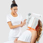 Esthetician in white uniform using LightStim ProPanel LED light therapy device on client's back, demonstrating professional s
