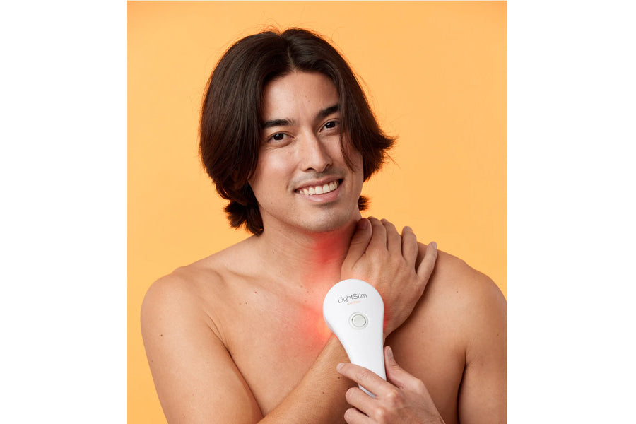 Man holding white LightStim LED pain relief device against shoulder showing red light therapy on skin against yellow backgrou