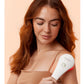 Woman with red hair holding white and red LightStim LED therapy device against shoulder on peach background