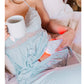 Light blue quilted device with orange LED panel worn on arm by model holding white mug