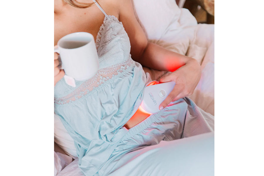 Light blue quilted device with orange LED panel worn on arm by model holding white mug