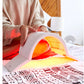 Lightstim Elipsa pink light therapy lamp with red and yellow LED glow, worn by model in beige sweater