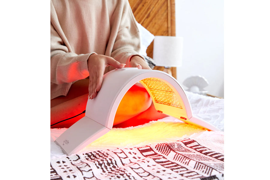 Lightstim Elipsa pink light therapy lamp with red and yellow LED glow, worn by model in beige sweater