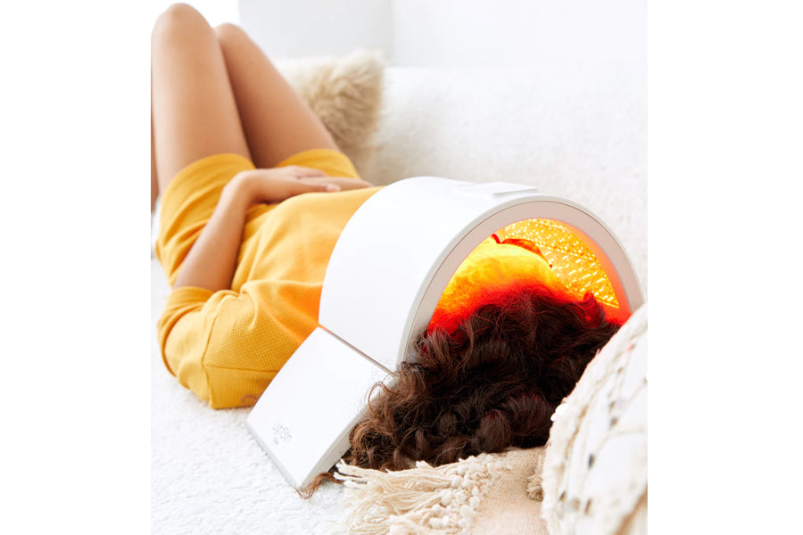 Woman wearing yellow socks using white Lightstim Elipsa light therapy face lamp with glowing red and yellow light panel on wh