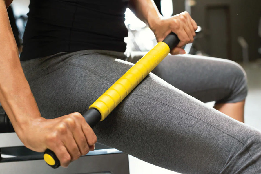 Person using yellow and black massage roller on gray leggings during workout