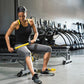 Woman using yellow and black massage bar on leg in gym setting with equipment in background